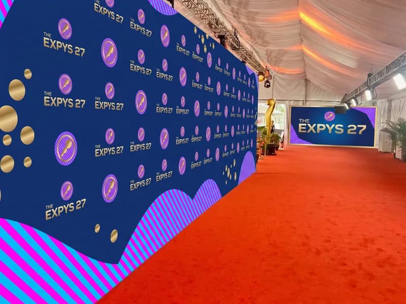 The Expys 27 media wall along a red carpet, gold marks on night ink under a lit marquee