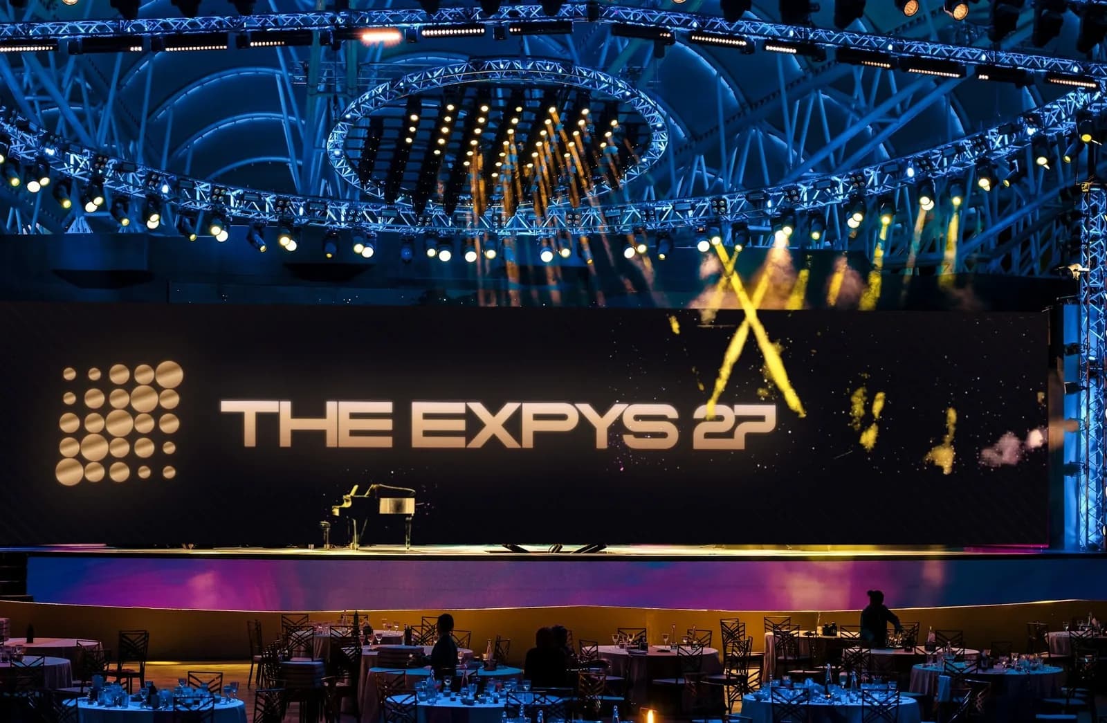 A stage under a lit truss dome, one LED wall the width of the stage showing THE EXPYS 27, rounds of ten below
