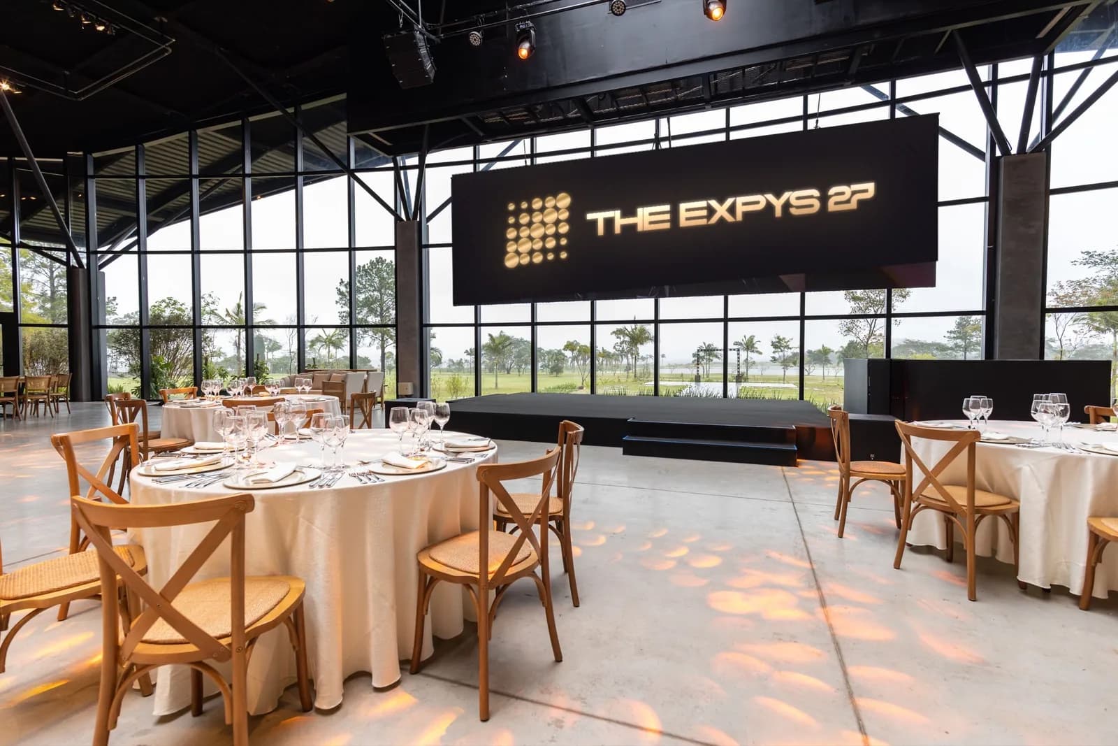 A glass-walled hall set for dinner, THE EXPYS 27 on the screen over the stage