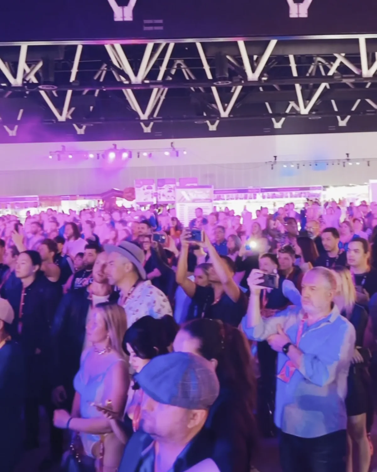 A standing crowd filming the stage on their phones under a triangular lighting rig