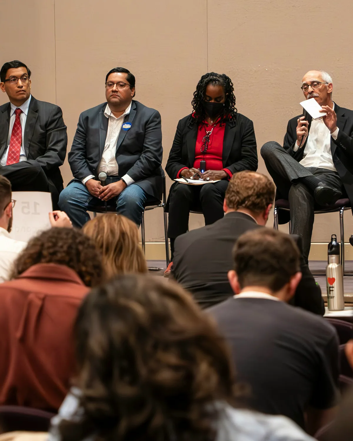 A panel of four in suits talking on a summit stage, the backs of the seated room in front of them