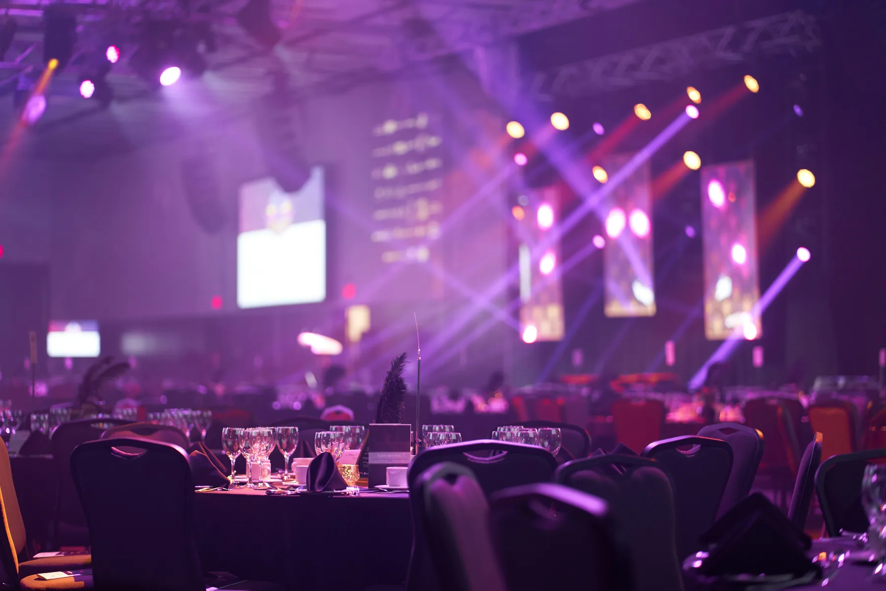 A ballroom set for an awards night, rounds of ten in the foreground and the stage lit violet beyond